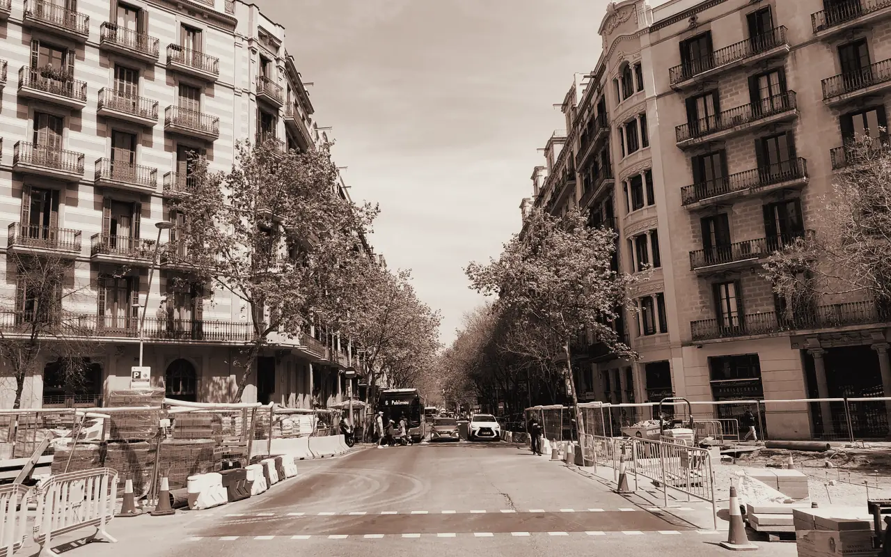 Calle del Eixample de Barcelona con edificios de balcones, plátanos y obras en la calzada.