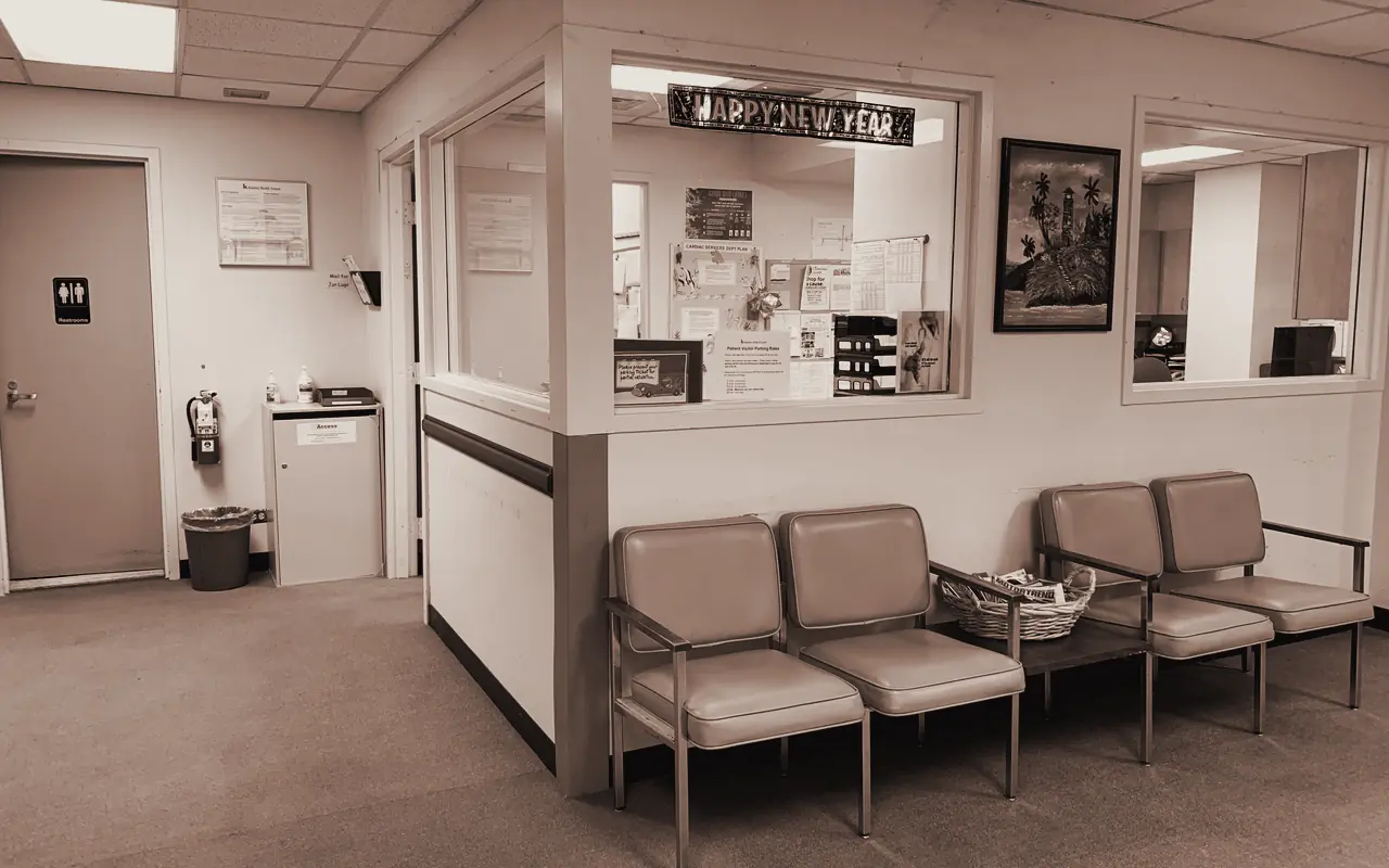 Sala de espera de una clínica con sillones tapizados y la ventanilla de recepción al fondo.