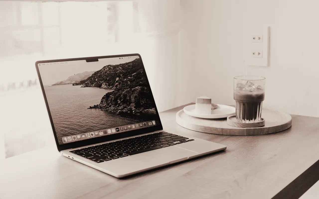 Un portátil abierto y una taza sobre una mesa clara, junto a la pared.